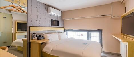 Una habitación de hotel moderna con una cama, mesita de noche, televisión y un armario con ropa colgada.