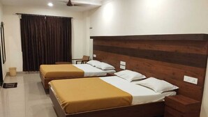 A hotel room with a large bed, two smaller beds, a wooden headboard, and a curtain. - Hotel Alankar (Nagercoil)