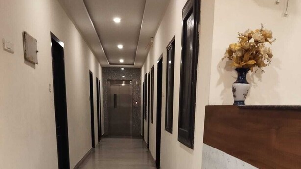 A long, narrow hallway with a tiled floor, doors on both sides, and a wooden counter with a vase of flowers on the right. - Hotel Alankar (Nagercoil)