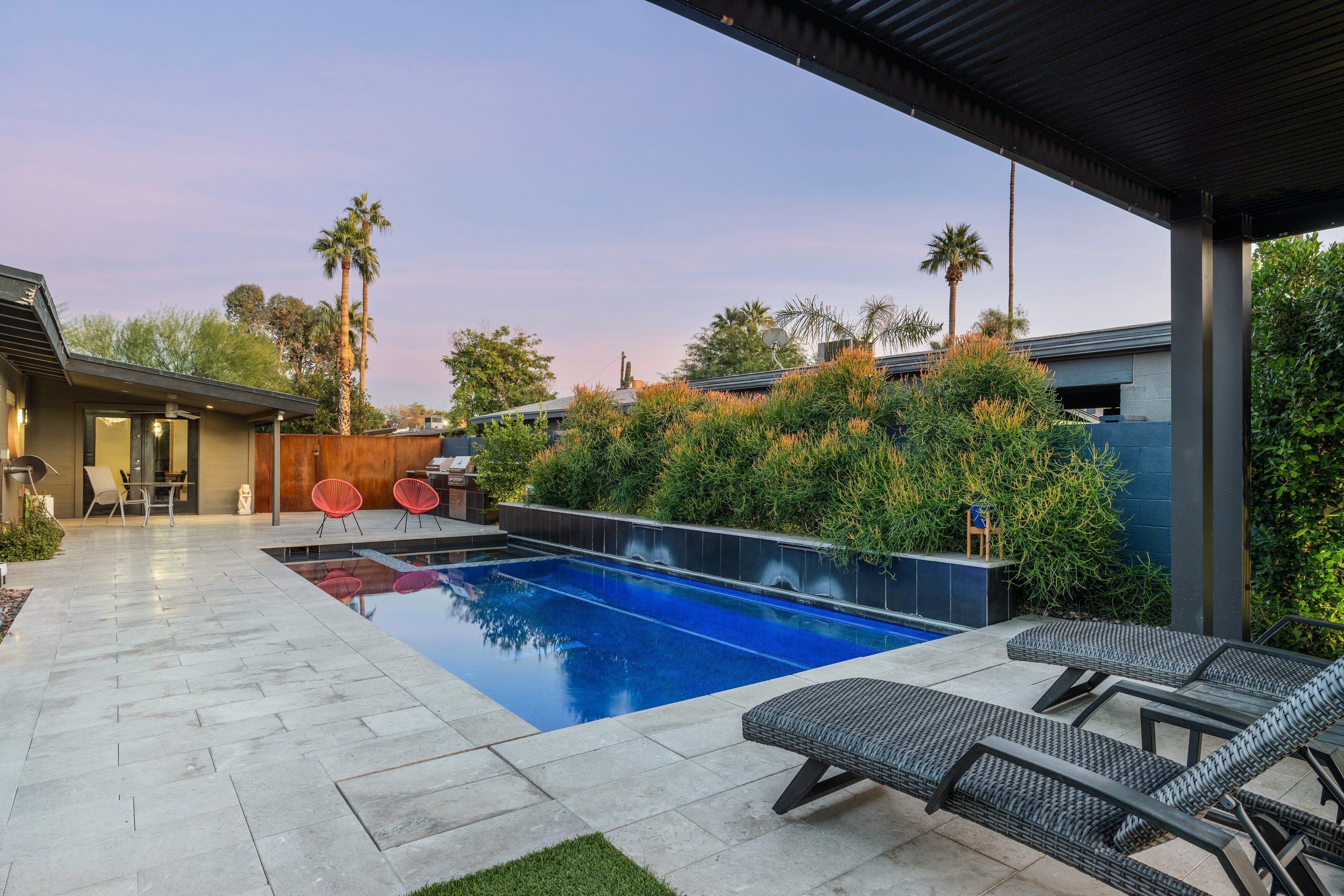 Un espace piscine extérieur moderne, doté de chaises longues, d’une table de patio et d’un coin salon abrité.