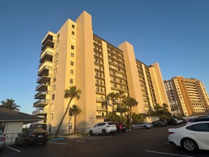 A multi-story hotel with balconies, a parking lot, and palm trees. - Direct oceanfront, corner balcony - amazing views ocean to river! On the beach!  (Fort Pierce)