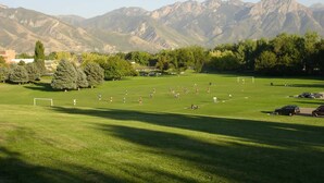 A soccer field with players and a goal, surrounded by trees and mountains.