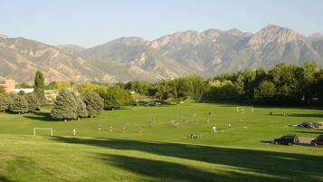 A soccer field with players and a goal, surrounded by trees and mountains.