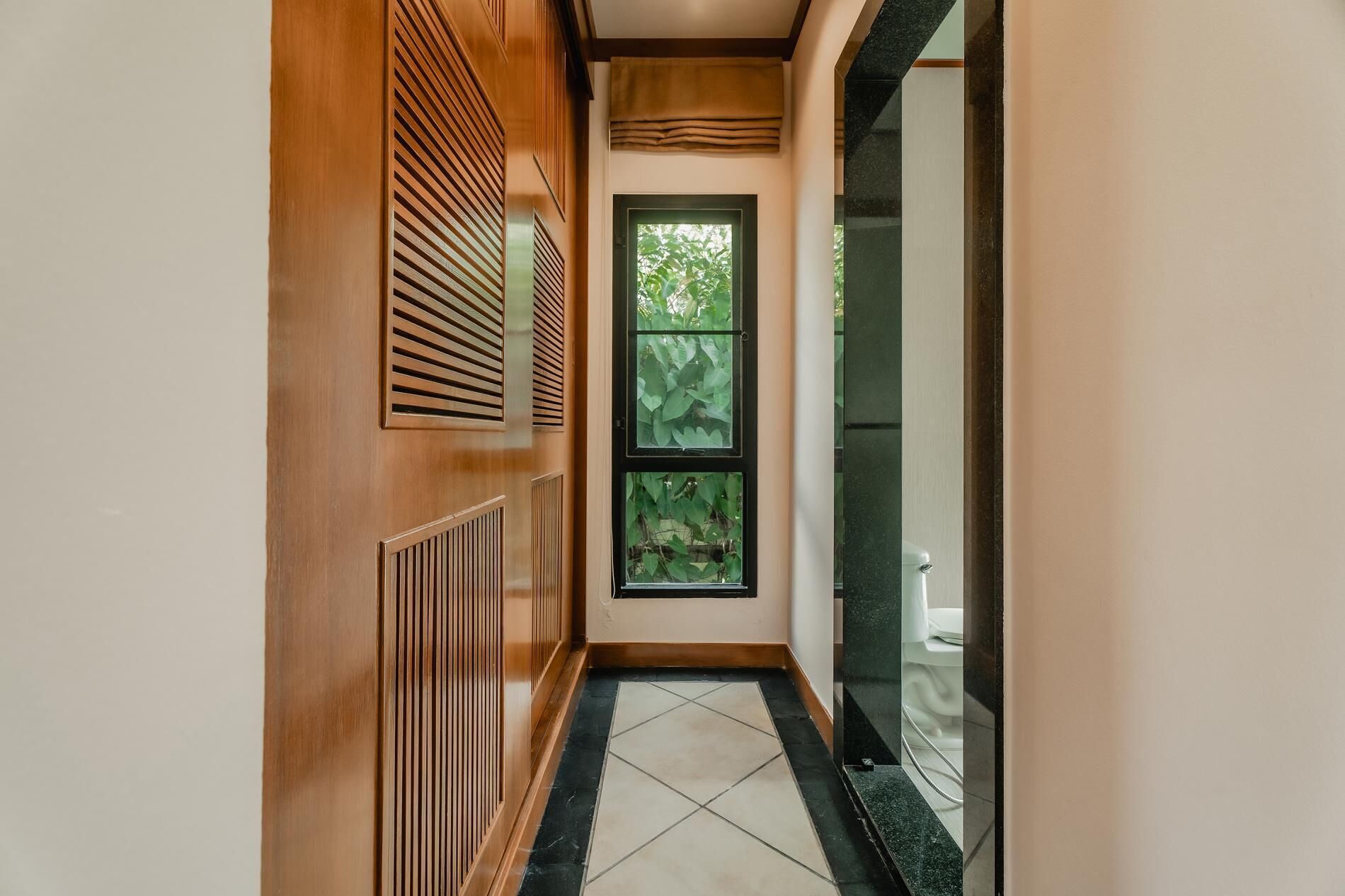 A hallway with wooden paneling, a tiled floor, and a window with a view of greenery.