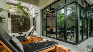 A modern room with a glass wall, a wooden bench, and a lounge chair. - Rose Pool Villa, The perfect private oasis (Rawai)