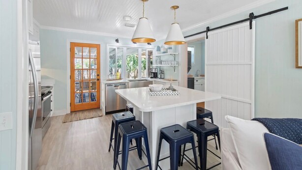 Una cocina moderna con armarios blancos, una isla central y taburetes de bar.