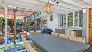 Un espacio de comedor al aire libre con techo, que incluye una mesa larga, sillas de mimbre, una pérgola y una lámpara colgante.