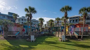 Un resort con edificios de varios pisos, palmeras y un espacio central abierto con un letrero que dice 'Artists of the Gulf Coast'.