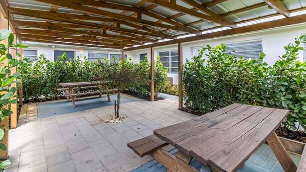 Un patio abrité avec une table en bois et des bancs, entouré d’une végétation luxuriante.