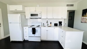 Une cuisine moderne avec des meubles blancs, un réfrigérateur blanc, un four à micro-ondes, une cuisinière et une machine à café.