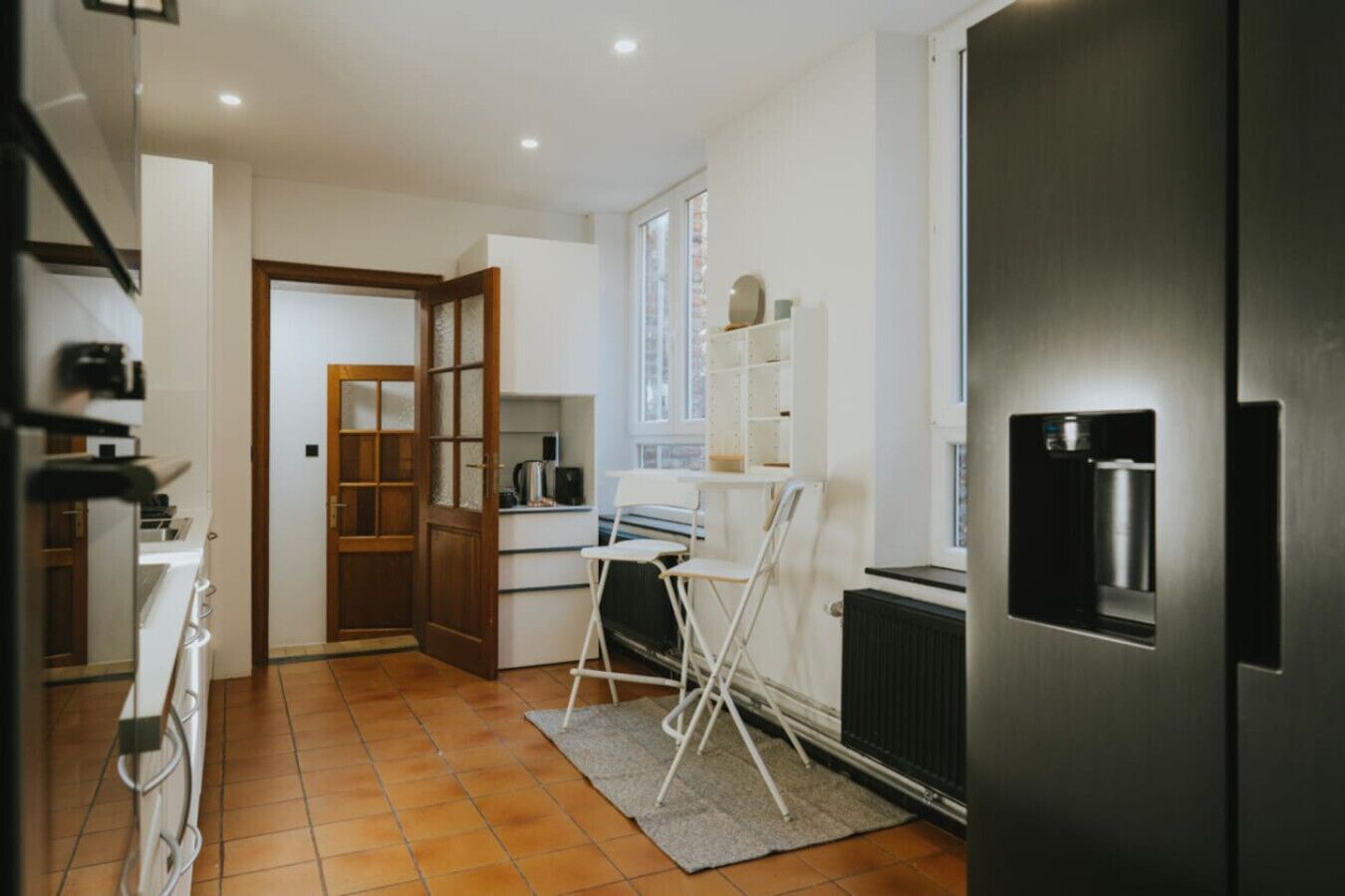 Een keuken met een koelkast, oven en een witte opklapbare stoel.