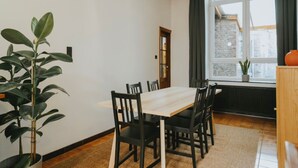 A dining area with a wooden table and chairs, a potted plant, and a window with a view of a brick building. - 2 bedroom apartment in Liege (Saint Leonard) (Liège)