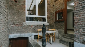 A small, enclosed patio area with a brick wall, a window, a fireplace, and a table with chairs. - 2 bedroom apartment in Liege (Saint Leonard) (Liège)