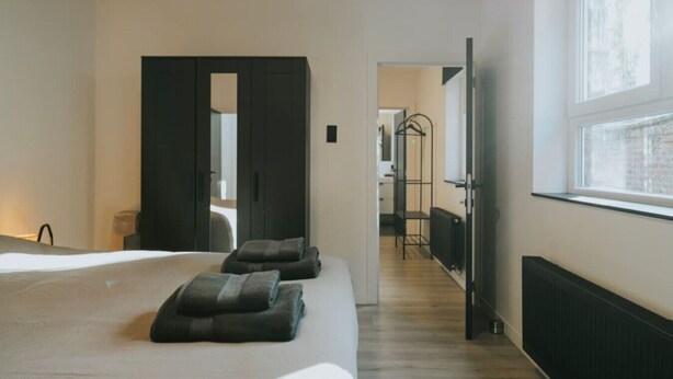 A modern hotel room with a large bed, a walk-in closet, a bathroom with a mirror, and a view of the city through the window. - 2 bedroom apartment in Liege (Saint Leonard) (Liège)