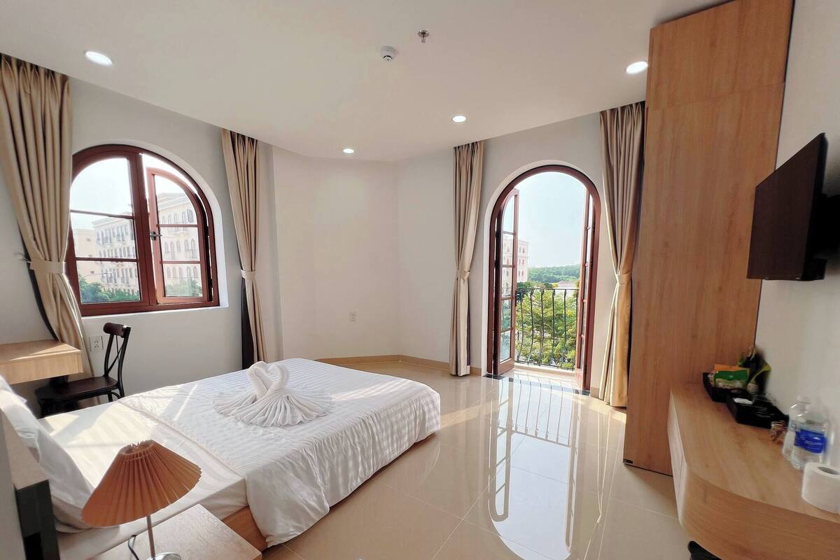 A hotel room with a bed, a desk, a chair, a TV, and a balcony with a view.