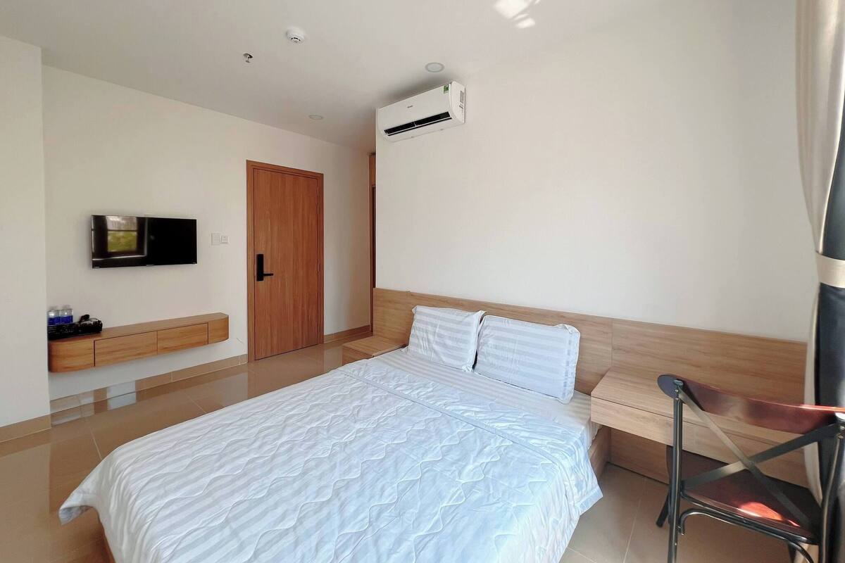 A modern bedroom with a bed, a TV, a wooden door, and an air conditioning unit.