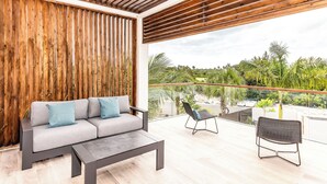 A modern outdoor lounge area with a wooden ceiling, a grey sofa with cushions, a small table, and two chairs. - Lotus Villas #1-Leeward Palms. Your Gateway to Paradise & Step into Serenity.... (Leeward Settlement)