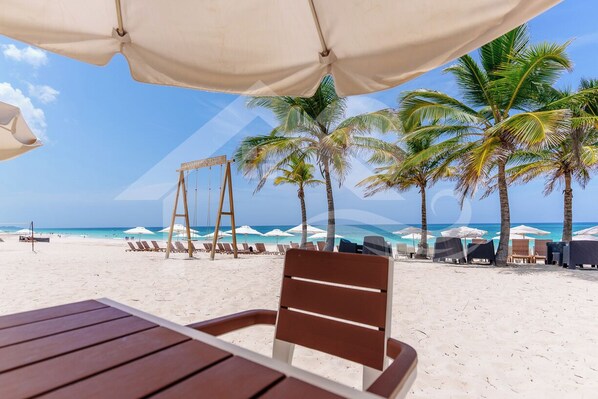 Une vue sur la plage avec une table et des chaises en bois, des palmiers et des parasols de plage.