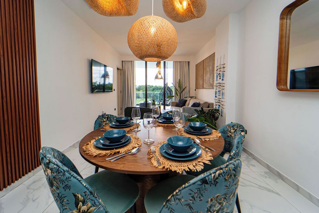 Un coin repas avec une table ronde dressée pour six personnes, entourée de six chaises à l’assise recouverte d’un tissu à motifs floraux.