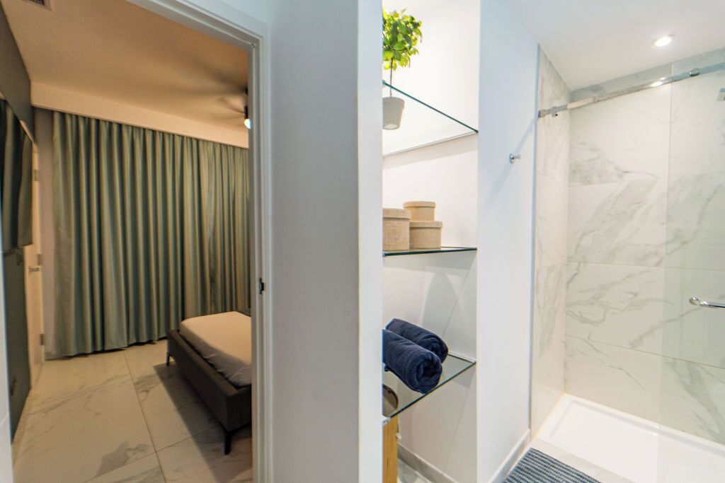 Ein modernes Badezimmer mit Duschkabine aus Glas, einem Bett mit weißer Matratze und einem Glastischchen mit Handtüchern.