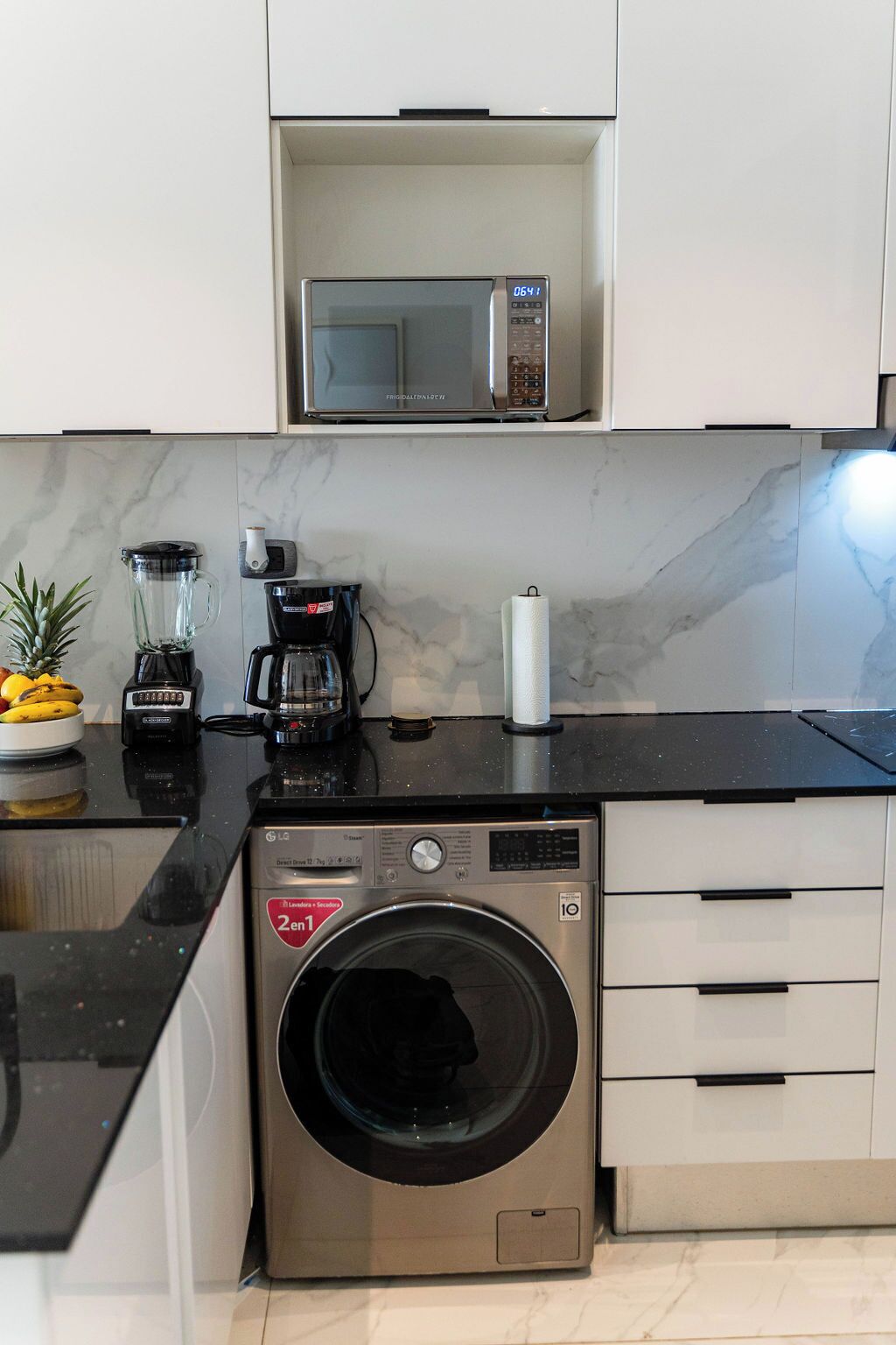 Uma cozinha compacta com micro-ondas, cafeteira, liquidificador e máquina de lavar.