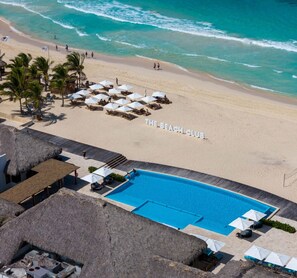 Un club de playa con piscina, sillas de descanso, sombrillas y palmeras.