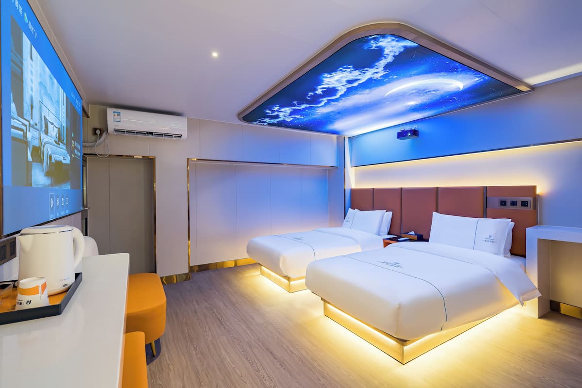 Een hotelkamer met twee bedden, een bureau met een koffiezetapparaat, een televisie en een plafond met een ontwerp gebaseerd op de ruimte.