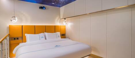 A modern hotel room with a bed, a night sky ceiling mural, and a wooden floor.