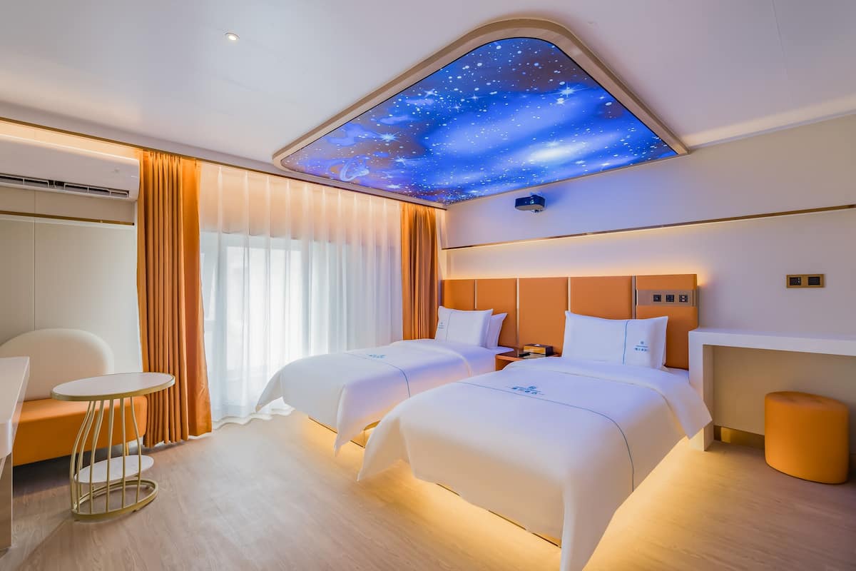 Een hotelkamer met twee bedden, een bureau, een stoel en een plafond met sterrenhemelmotief.