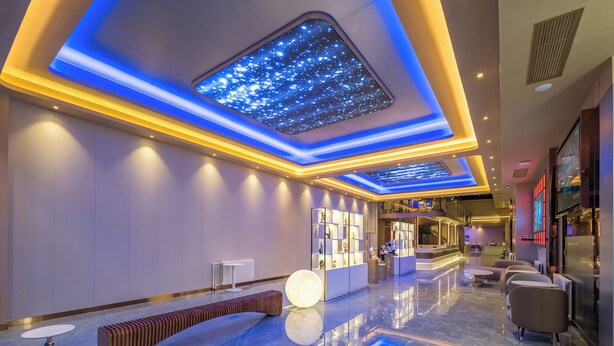 Un moderno vestíbulo de hotel con piso reflectante, un área de descanso central y un techo con detalles de luces que simulan estrellas.