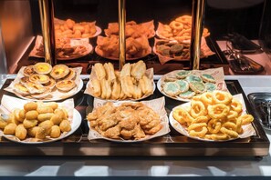 Un buffet proposant une variété de plats frits, notamment des pâtisseries, du pain et des rondelles d’oignon.