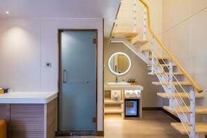 Een moderne badkamer met een glazen deur, een ronde spiegel en een houten trap.