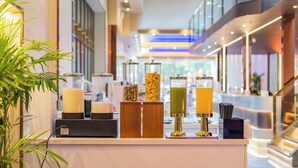 Zona de recepción de hotel con un mostrador que ofrece diversos servicios, como una máquina de café, dispensador de zumo y dispensador de agua.