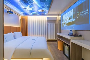 Quarto de hotel com uma cama grande, projeção de espaço no teto, televisão de tela plana e mesa de cabeceira com uma garrafa de água.