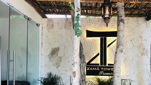 Un edificio moderno con fachada de piedra y entrada de vidrio, con un cartel que dice "ZAMÁ TOWER".