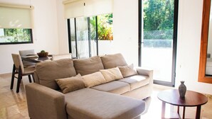Una sala de estar moderna con un sofá seccional color crema, una mesita redonda con un florero, y un comedor con mesa y sillas.