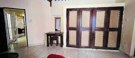 A room with a tiled floor, a red cushioned chair, a small table, and a large wooden door with a woven screen.