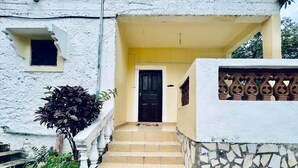 Una escalera conduce a una puerta con un pequeño ventanal, rodeada de plantas y un muro decorativo.
