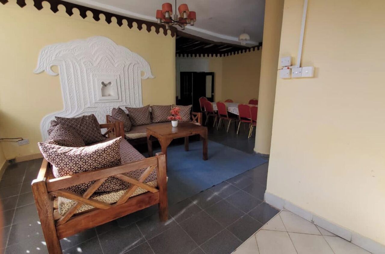 Zona pranzo con tavolo e sedie in legno, un divano con cuscini decorati e un elemento decorativo a parete.