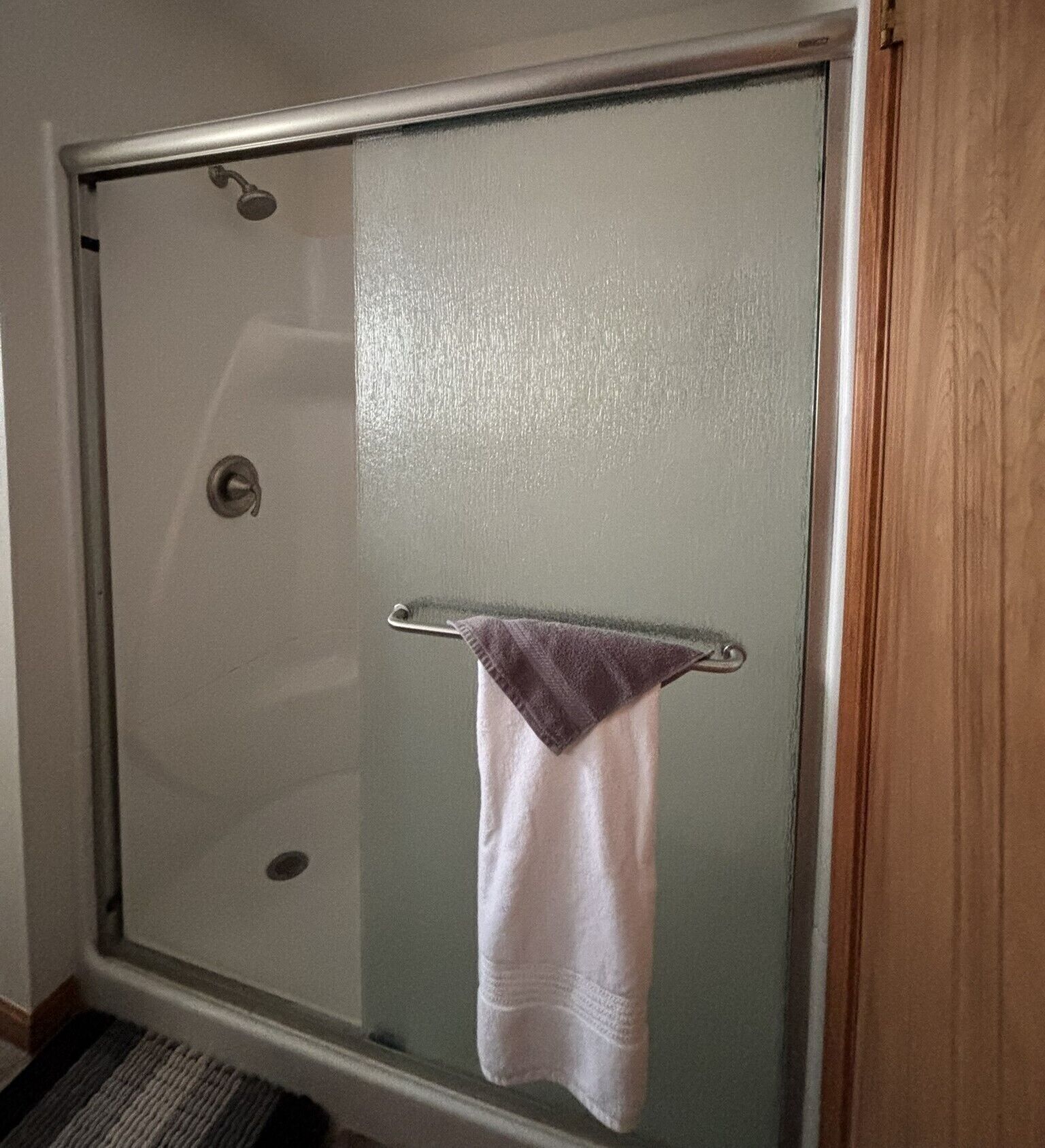 Une douche fermée par des parois de verre, avec un porte-serviettes et une serviette blanche qui y est suspendue.