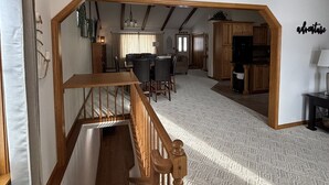 A spacious loft-style living area with a high ceiling, wooden staircase, and a dining area. - Live & Love Life on the Lake at Sunset Peak! (Howe)