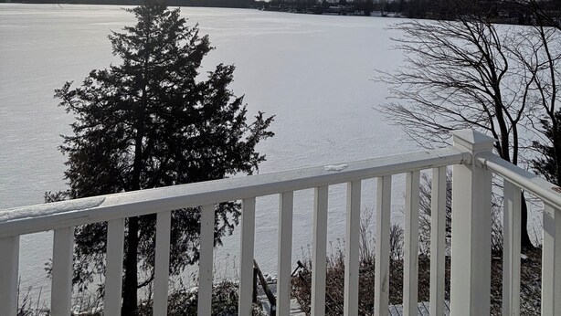 A view from a balcony overlooking a frozen lake with bare trees and a clear sky. - Live & Love Life on the Lake at Sunset Peak! (Howe)