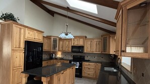 A kitchen with wooden cabinets, a black countertop, a stainless steel sink, and a skylight. - Live & Love Life on the Lake at Sunset Peak! (Howe)