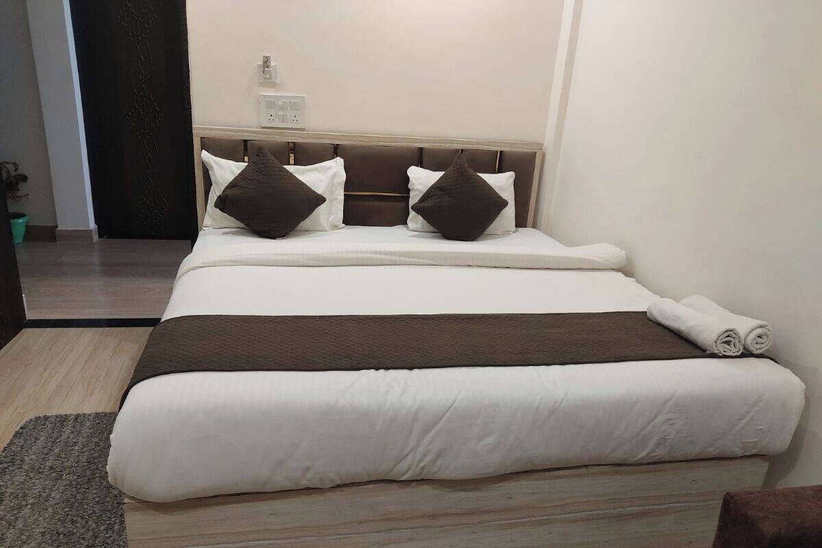 Een net opgemaakt bed met een hoofdbord, een nachtkastje met een lamp en een kleine bloempot.