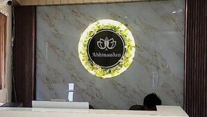 A reception desk with a marble wall background and a logo. - Hotel Abhinandan (Ayodhya)