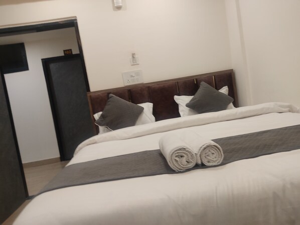 Habitación de hotel con una cama bien hecha, un cabecero de madera y una puerta que da a otra estancia.