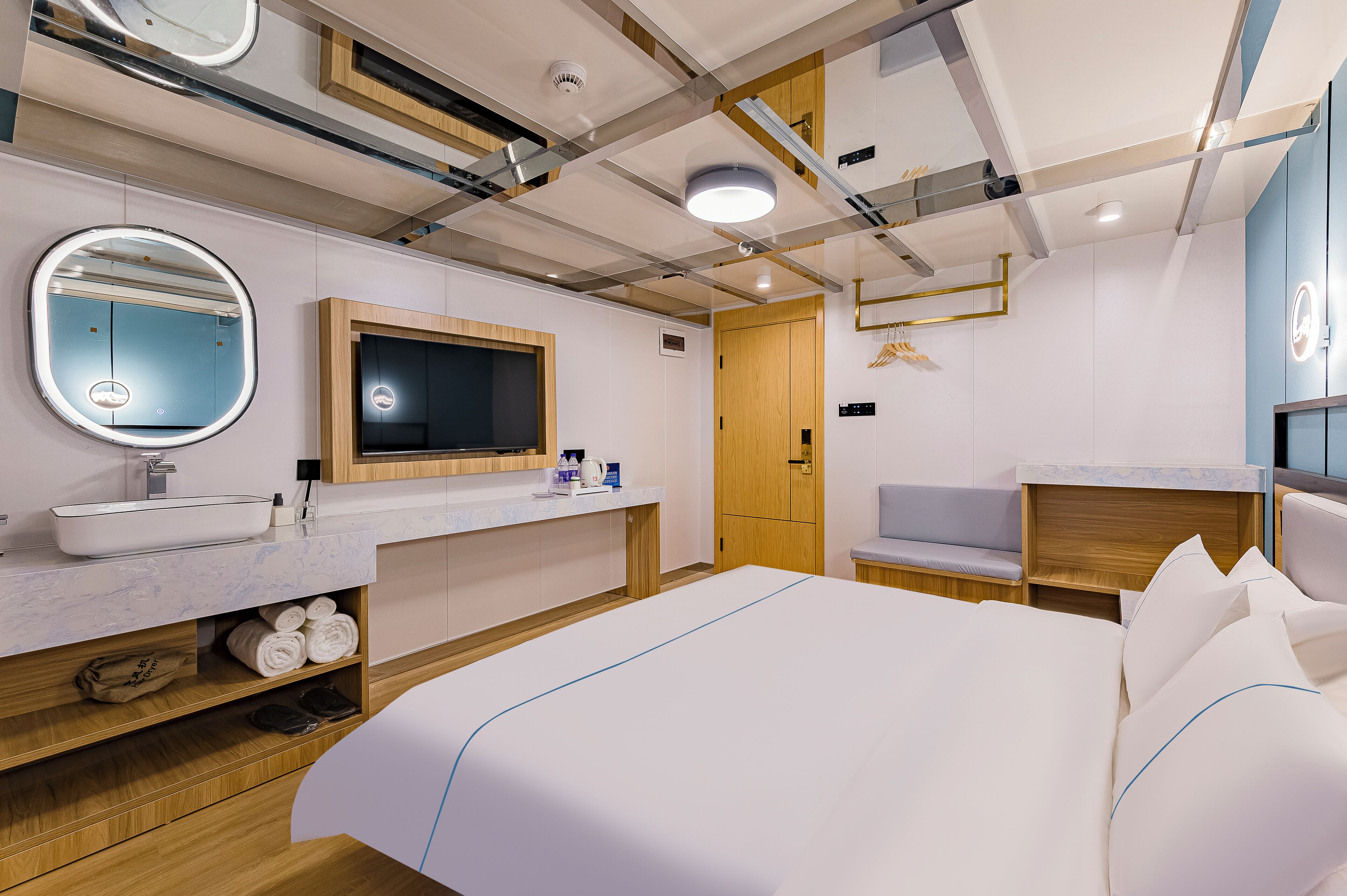 A modern hotel room with a large bed, a round mirror, a TV, and a wooden wardrobe.