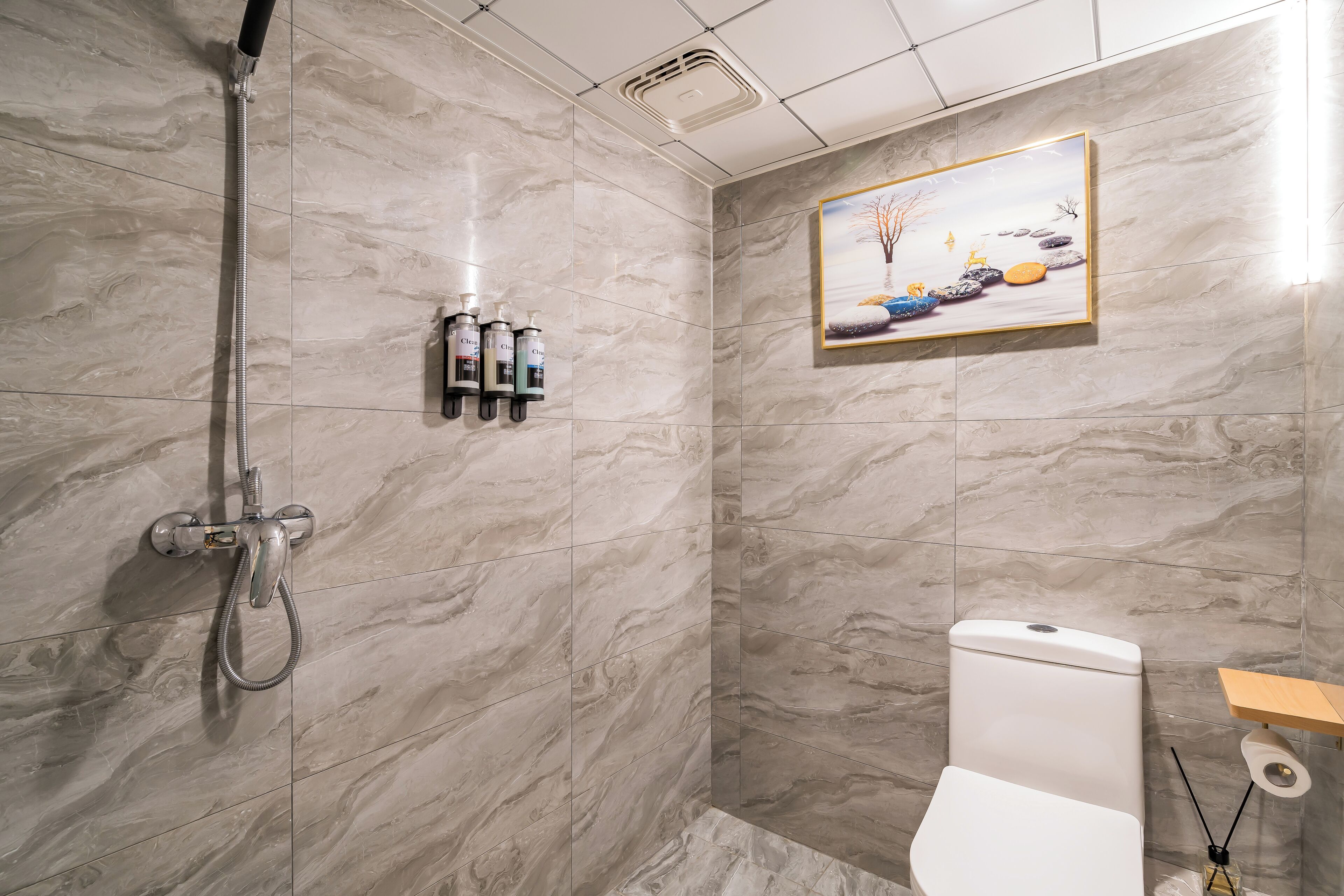 A bathroom with marble tiles, a shower, a toilet, and a shelf with toiletries.