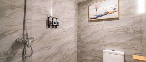 A bathroom with marble tiles, a shower, a toilet, and a shelf with toiletries.