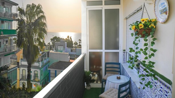 A balcony with a view of the sea, a table with chairs, and a hanging plant with sunflowers. - Fuente de Piedra Apartment (Torre Del Mar)